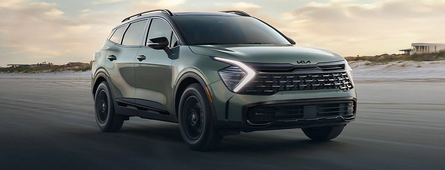 A green 2025 Kia Sportage driving on the beach
