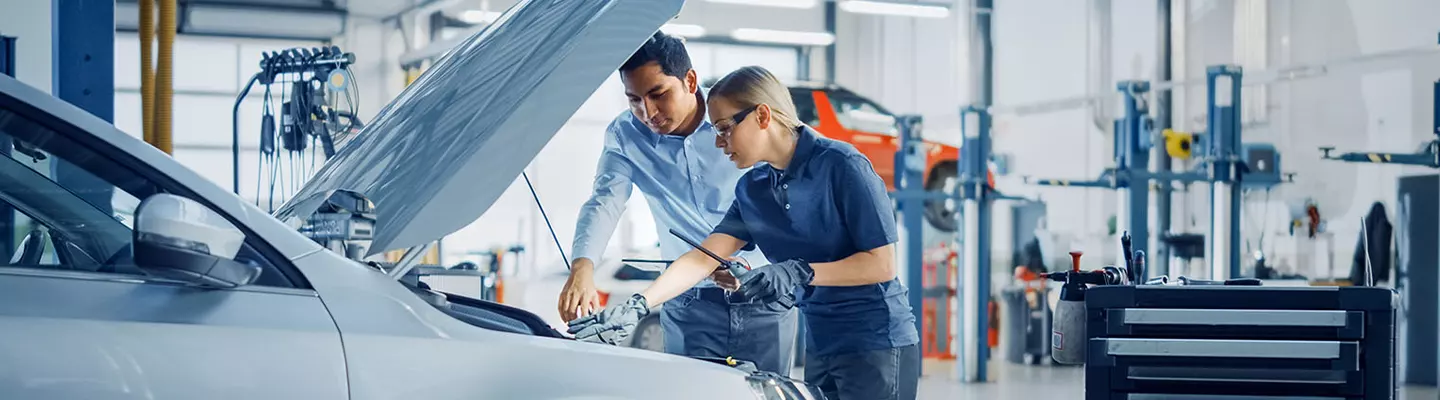mechanic and tech working under a hood of a car