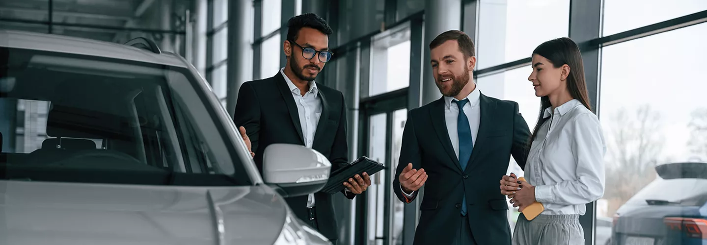 Car dealership sales consultant helping customers compare SUV features and explore vehicle options in a modern showroom
