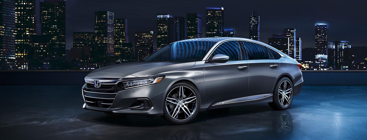 Silver 2022 Honda Accord parked at top building at night with city skyline behind