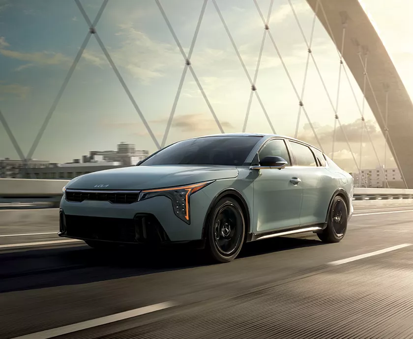 light blue Kia K4 crossing a bridge exterior shown from a three-quarter angle