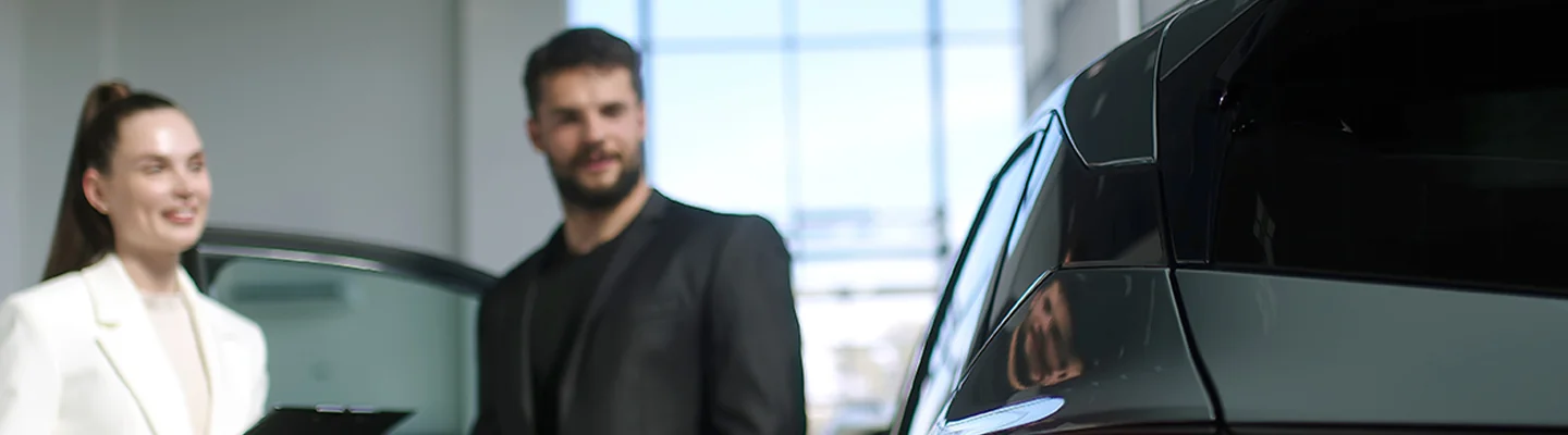 two people smiling and looking over car in dealership showroom