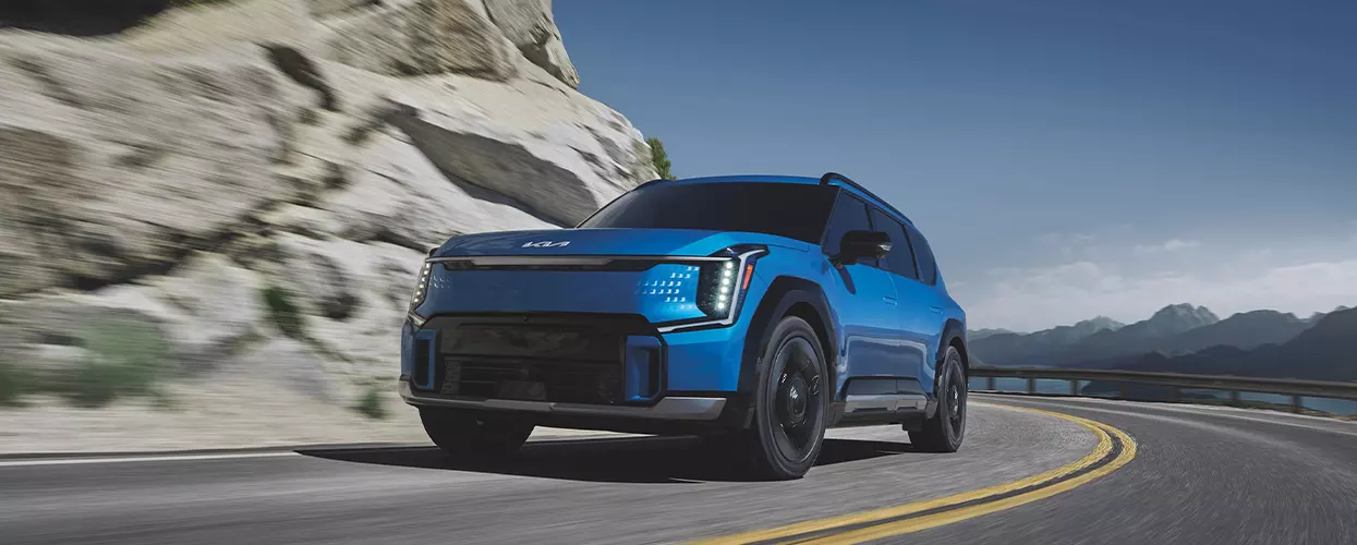 front view of a blue Kia SUV taking a corner on hilly road