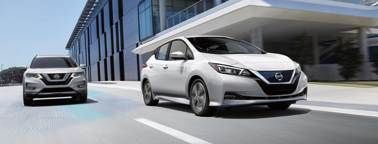 White 2022 Nissan Leaf driving next to a building