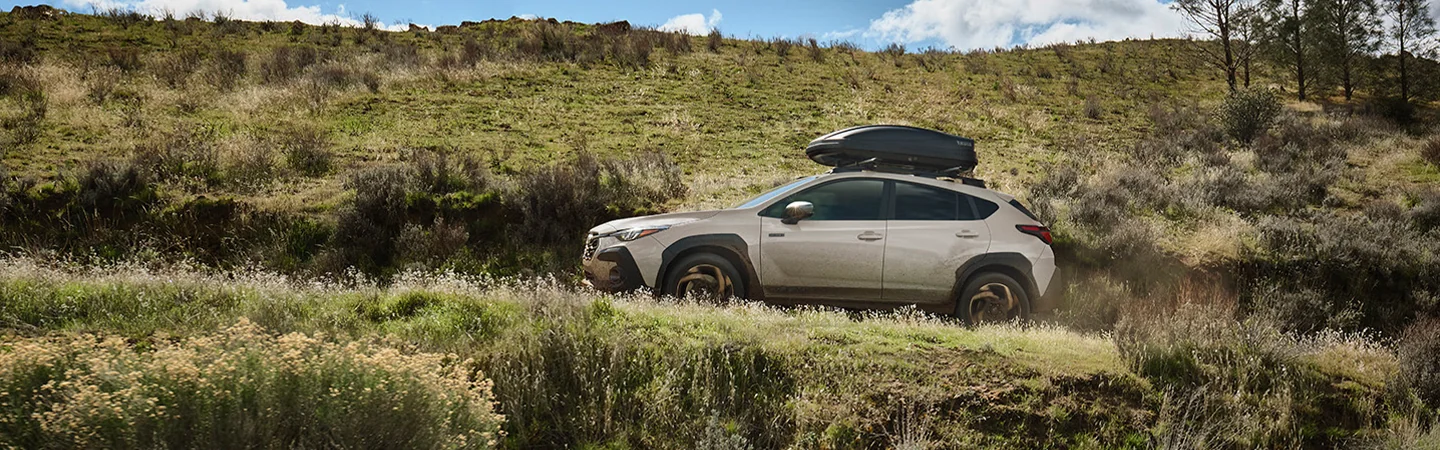 2026 Subaru Crosstrek Hybrid Sport with roof racked luggage driving offroad up hill