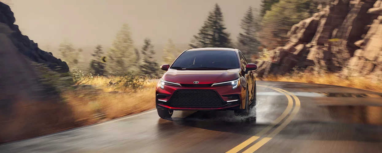 a red toyota sedan on country road turn in motion