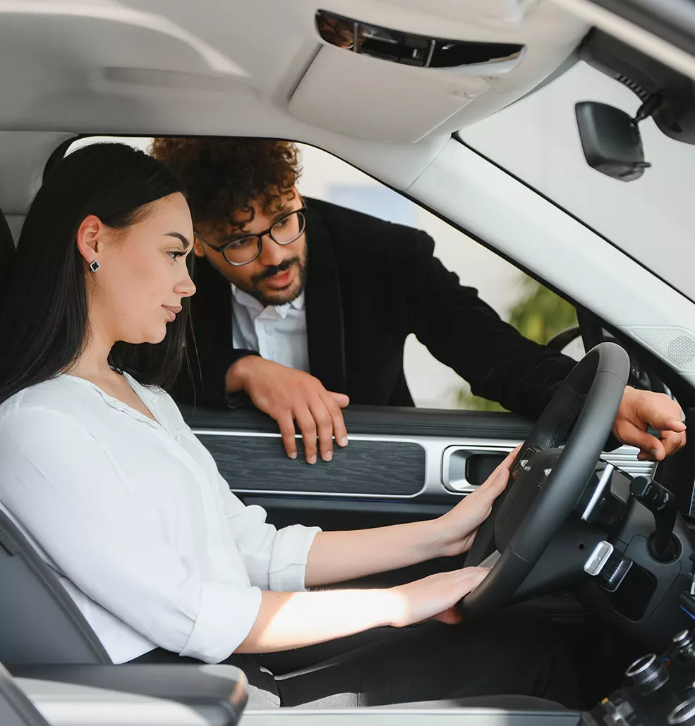 a driver seen in a 2026 Toyota RAV4 with interior technology in foreground and car salesperson at the window