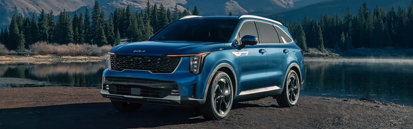 Front view of a blue  2025 Kia Sorento Hybrid parked by a lake with mountains in the background