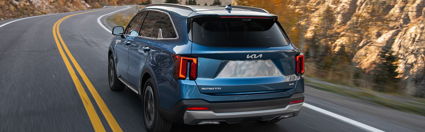 Rear view of a 2025 Kia Sorento Hybrid driving on a road in the wilderness