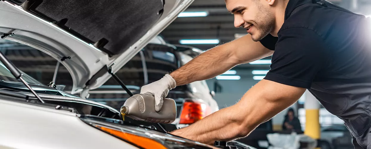 car mechanic pouring fluids into an engine at a dealership