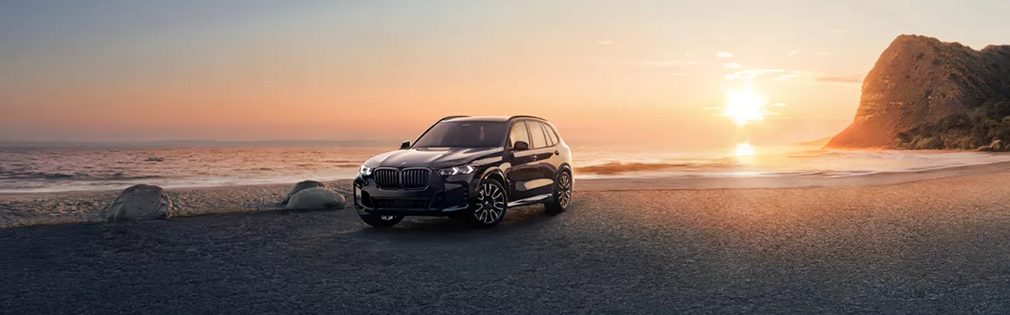 2026 BMW X5 parked on a beach with the sunset in the background