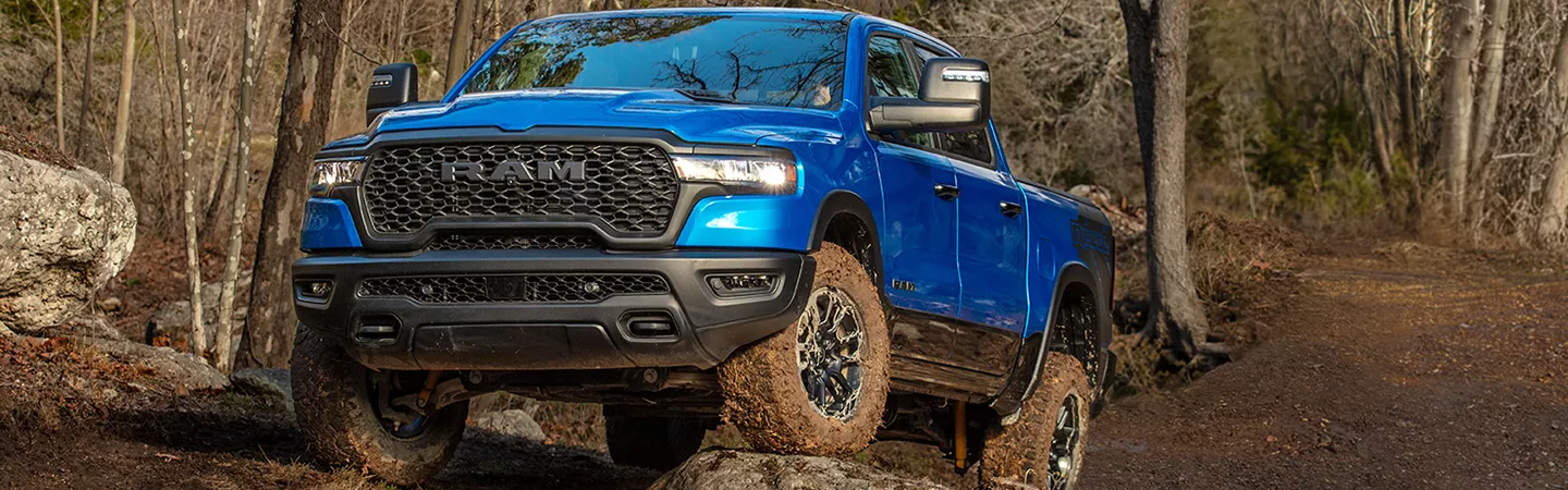 Front view of a blue 2026 RAM 1500 driving over rocks on a mountain