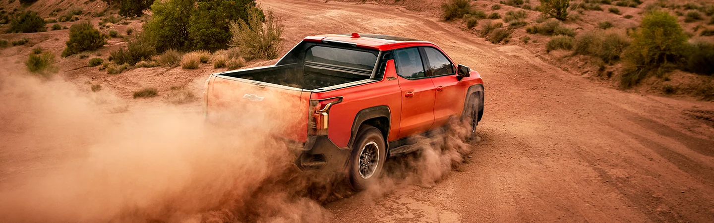 Rear view of the 2026 Chevrolet Silverado EV driving on a desert canyon road with dust in the air