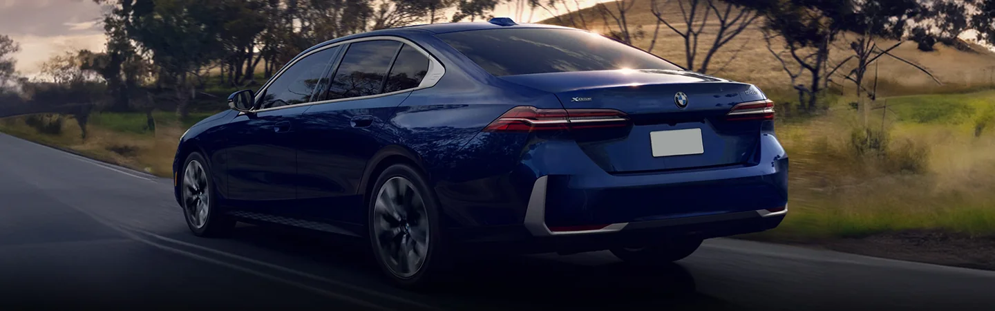 back view of a blue 2025 BMW 5 Series driving down the road