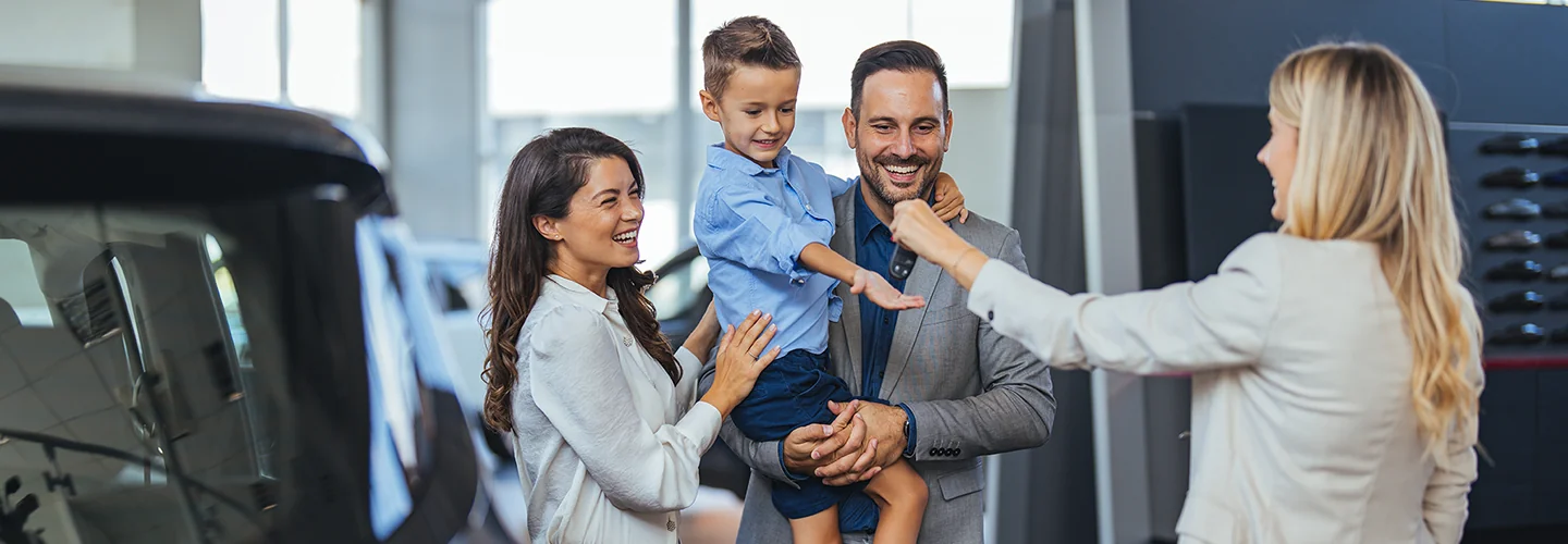 family of three smiling being given keys to their new Toyota