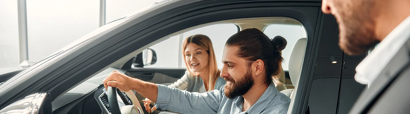 view of couple sitting in car in showroom talking with car sales person standing next to car