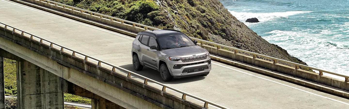 Side view of a blue 2025 Jeep Compass driving up a dirt hill