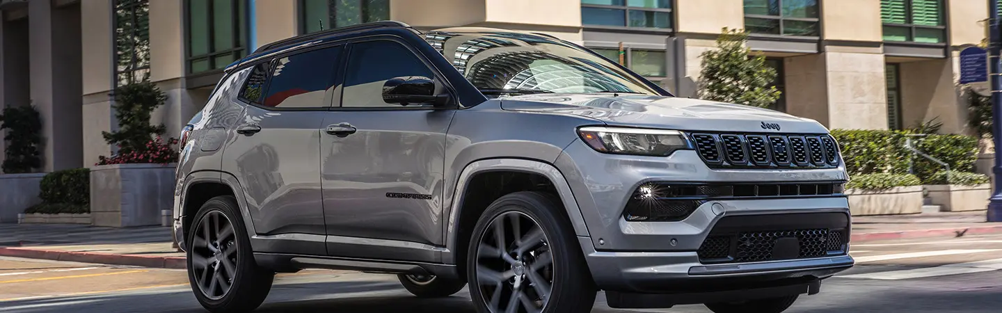 A white 2025 Jeep Compass driving down a hill