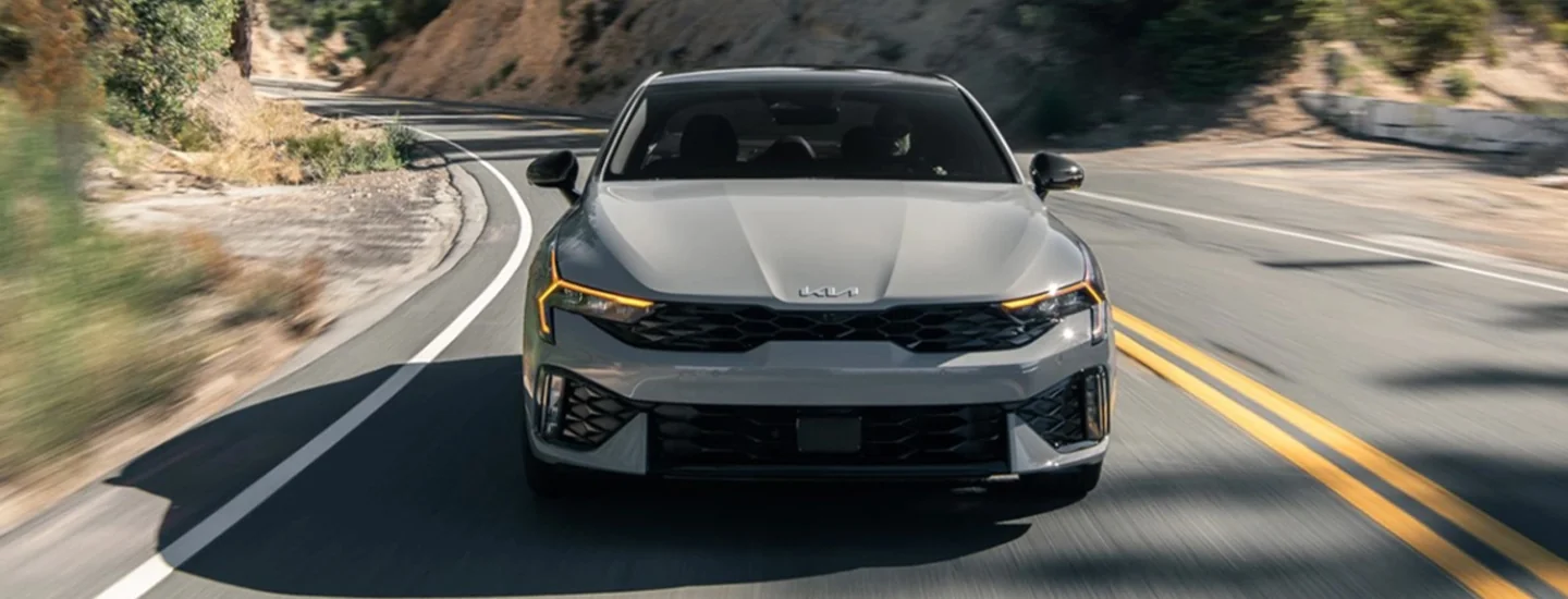 Front view of a gray 2025 Kia K5 driving on a mountain road