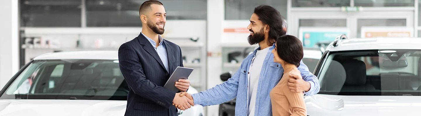 Hyundai salesman shaking hands of man that is holding on to his wife while standing in the dealership