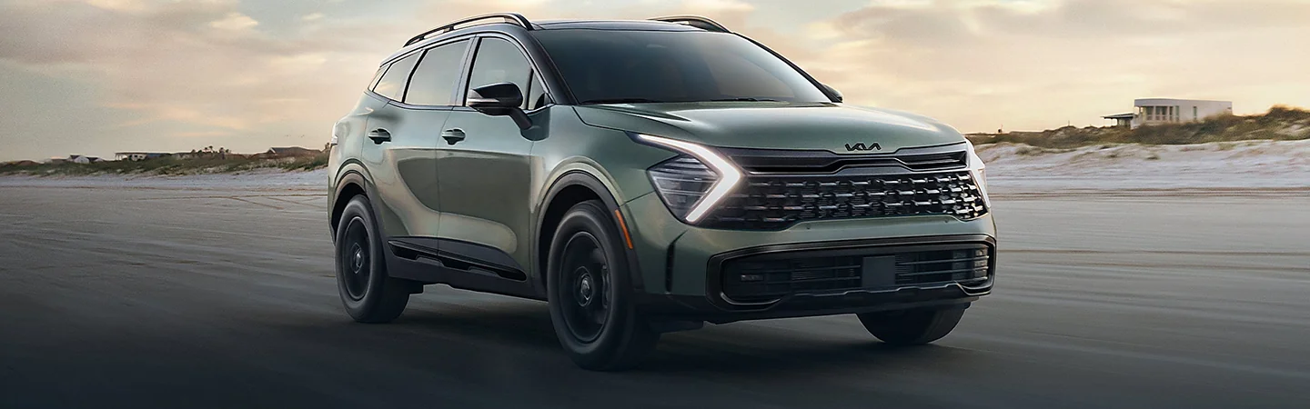 Front side view of a green 2025 Kia Sportage driving on the beach