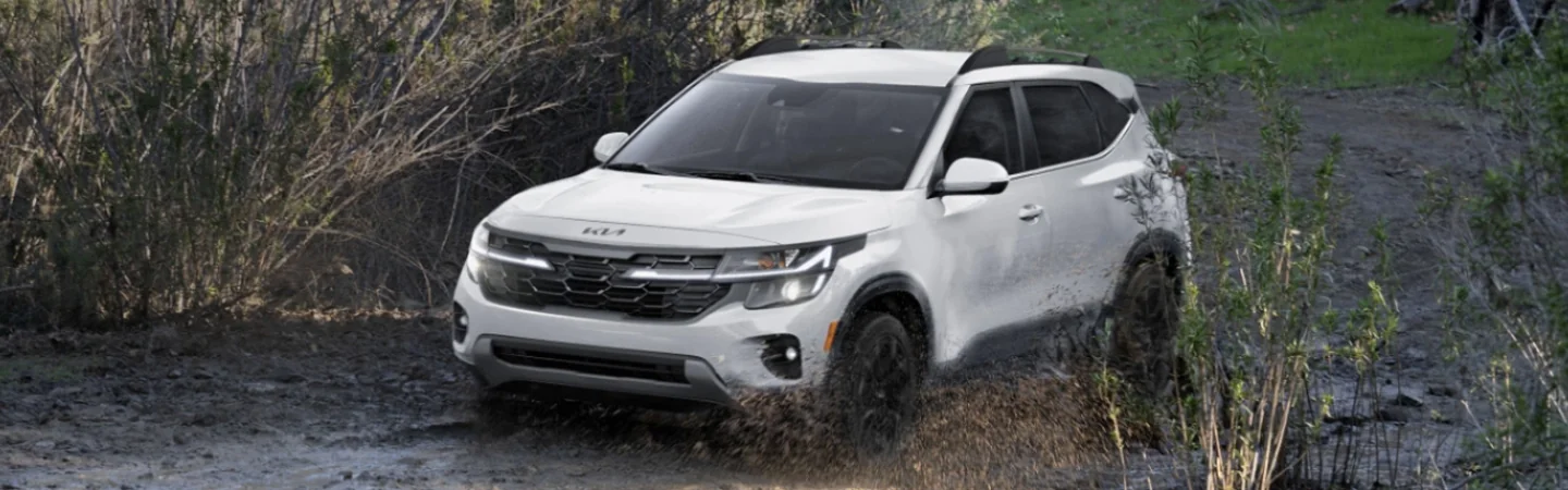 A white 2025 Kia Seltos driving in mud