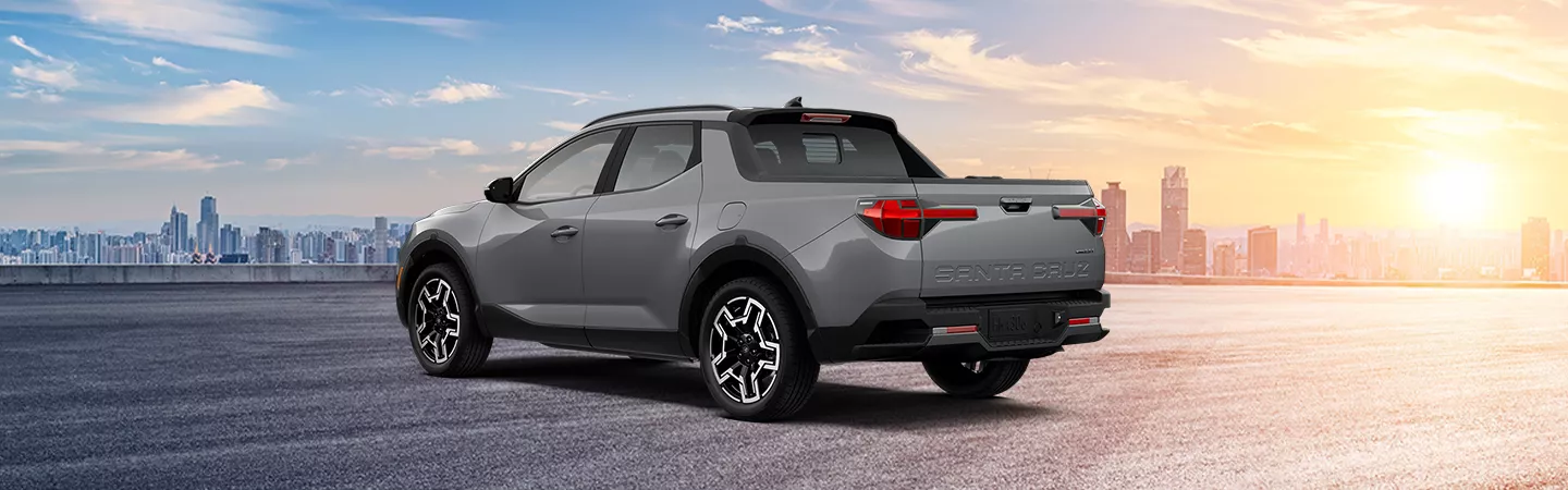 Rear view of 2026 Hyundai Santa Cruz pared in front of a city skyline at sunset