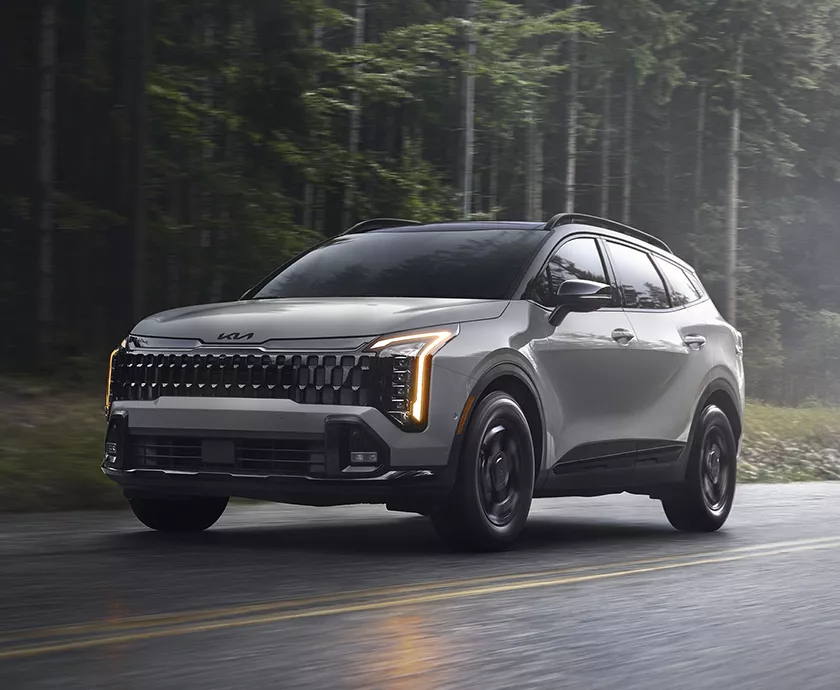 Front view of a gray 027 Kia Sportage driving on a road in the forest