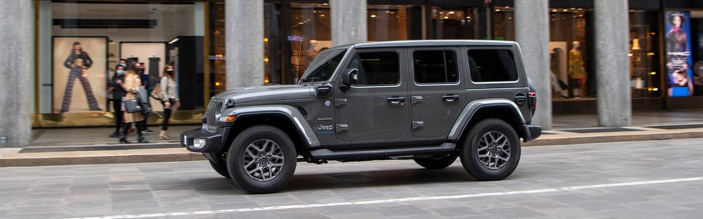 Side view of a grey Jeep Wrangler driving through the city.