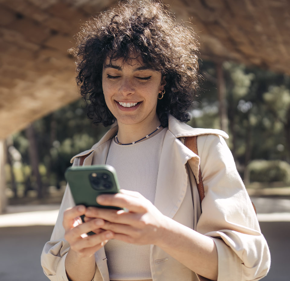 young woman smiling looking at her phone with view under a bridge behind her