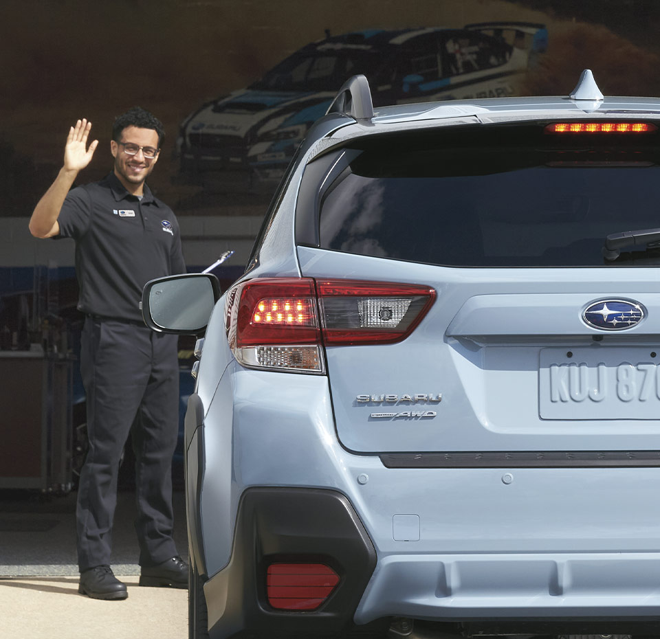 mechanic waving as Subaru driver reverses with view of rear of vehicle