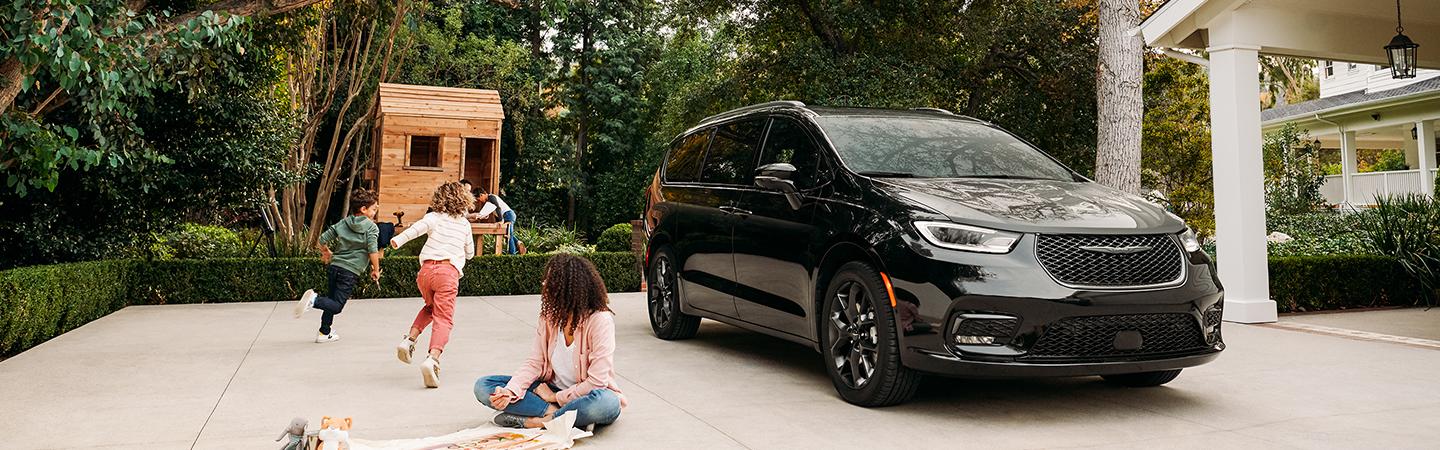 black 2021 Pacifica parked at house in driveway with children playing around it with wooden fort in yard in distance