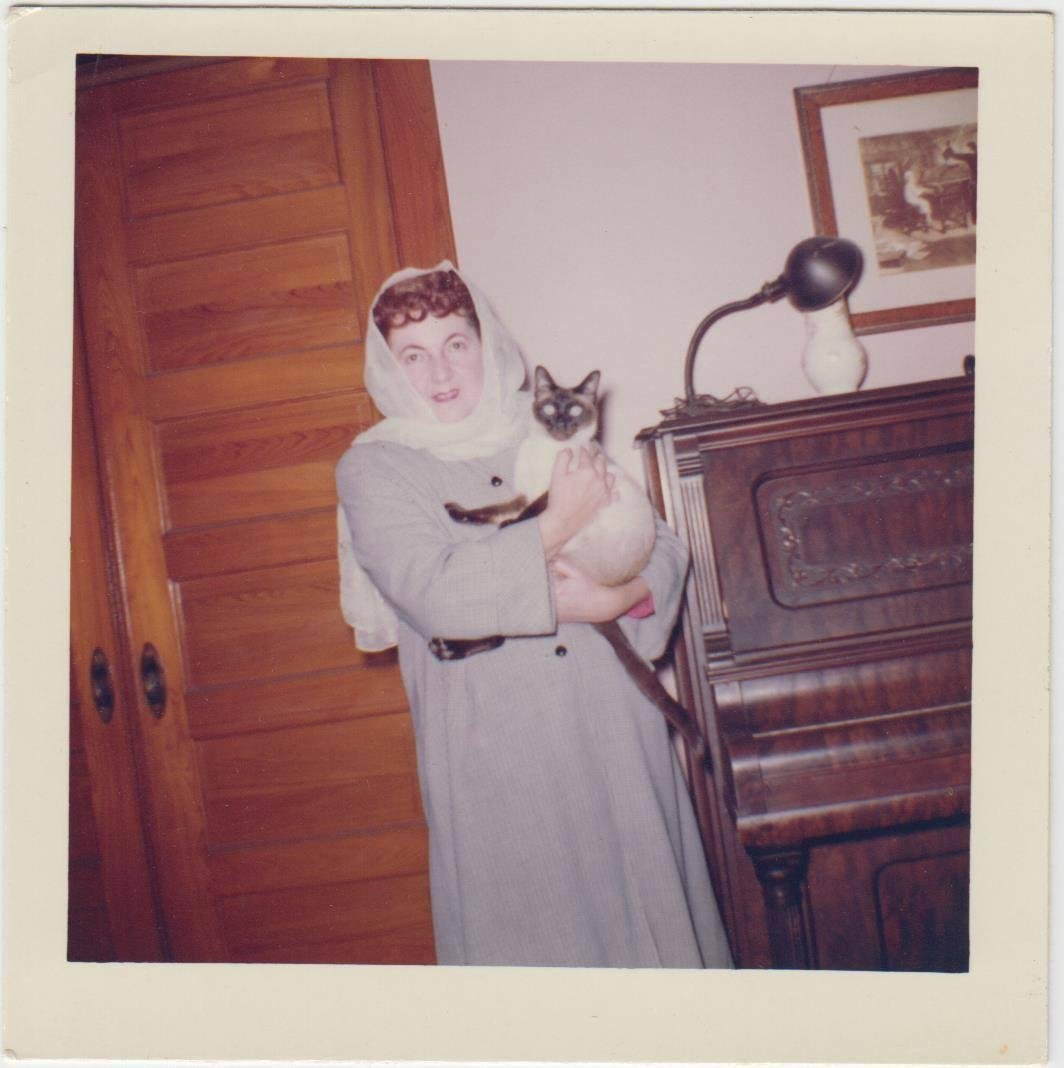 Mom at Aunt Kate's. That is her Siamese, one of two. Taken in the front parlor. Note piano, where I learned to love to play, The picture above the piano is of the child prodigy, W.A.Mozart - Composer, caught by his father a
