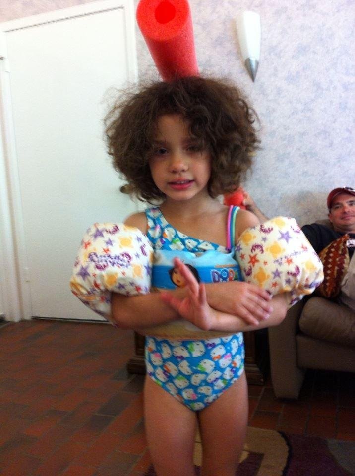 Maya is 5. She loves to swim. She has a noodle on top of her head.