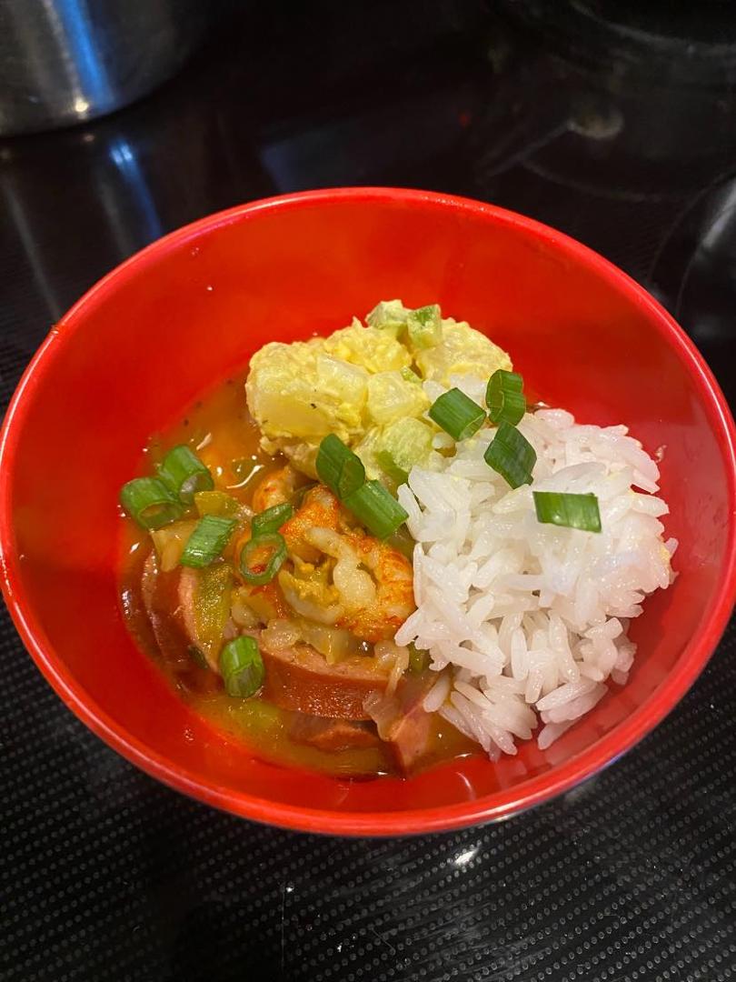 Authentic Louisiana crawfish gumbo accompanied by andouille sausage, potato salad, and a side of rice.