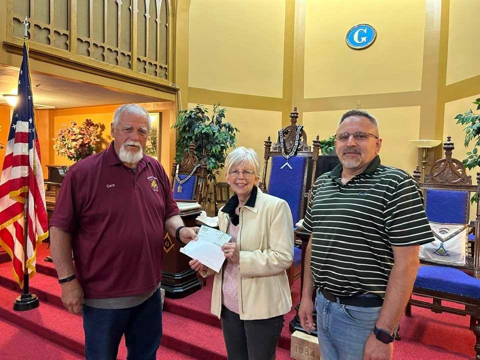 Buchanan Masons present Mary Lister a check of $1000.00 for their project of repairing the sidewalk at the Roti Roti Art Center. This will help defray a small portion of the amount needed to complete the repair. Presenting 