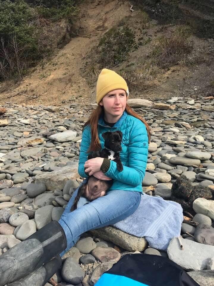 Emily on the Pacific Coast holding a foster dog while Dave surfs the waves.