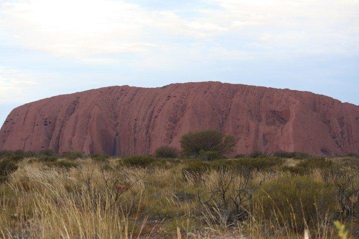 This mammoth rock rises out of the completely flat desert floor and shows a red color. We're told that the part we see above ground represents only one fourth of the rock. The other three fourths is below ground.