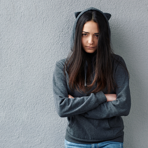A girl in hood with cat's ears crossing her arms, looking unhappy.