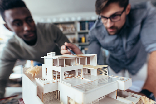 Close up shot of scale model house on table with architects. Two architects making architectural model in office together.
