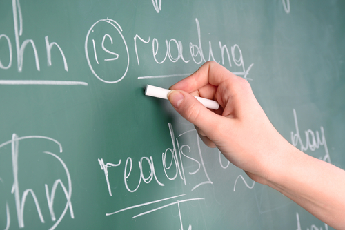 Teacher hand writing grammar sentences on blackboard background