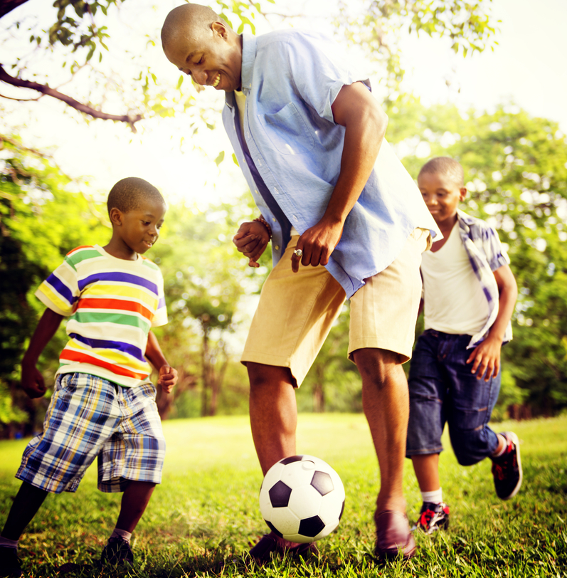 Two kids playing soccer with father