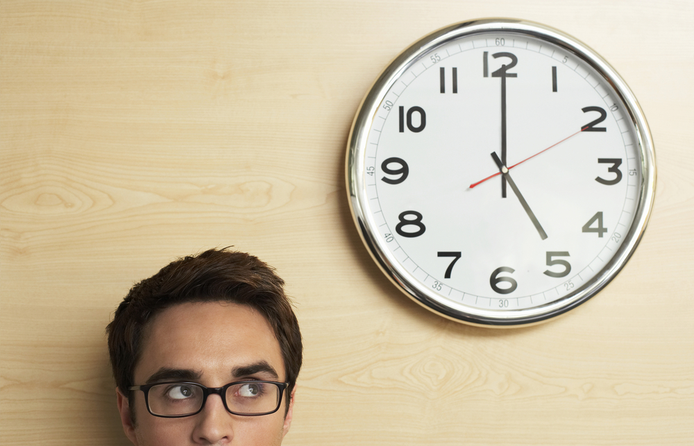 Young person wearing glasses looking at the clock on the wall in their office.