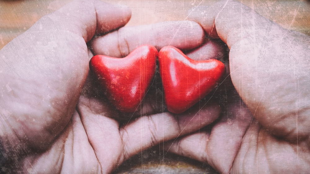 Hands holding two small red heart objects.