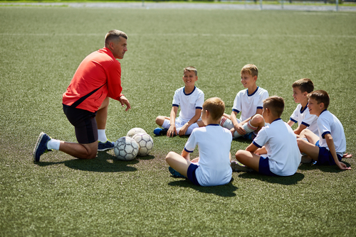 Portrait of boys sitting in front of coach on football field listening to pre game lecture