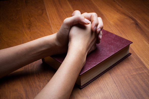 hands folded in prayer over a book