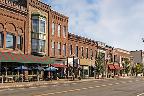 A photo of a typical small town main street in the United States of America. Features old brick buildings with specialty shops and restaurants. Decorated with autumn decor.