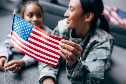 african american daughter and mother in military uniform with american flag at home.