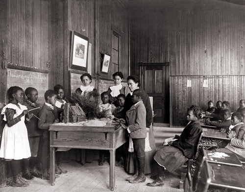 African American children learning about Thanksgiving, with model log cabin on table, Whittier Primary School, Hampton, Virginia. Ca. 1899.