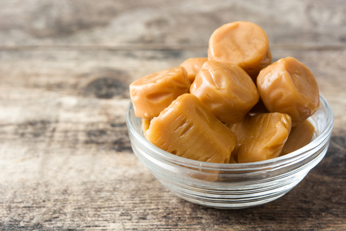Toffee caramel candies in a crystal bowl on wooden table.